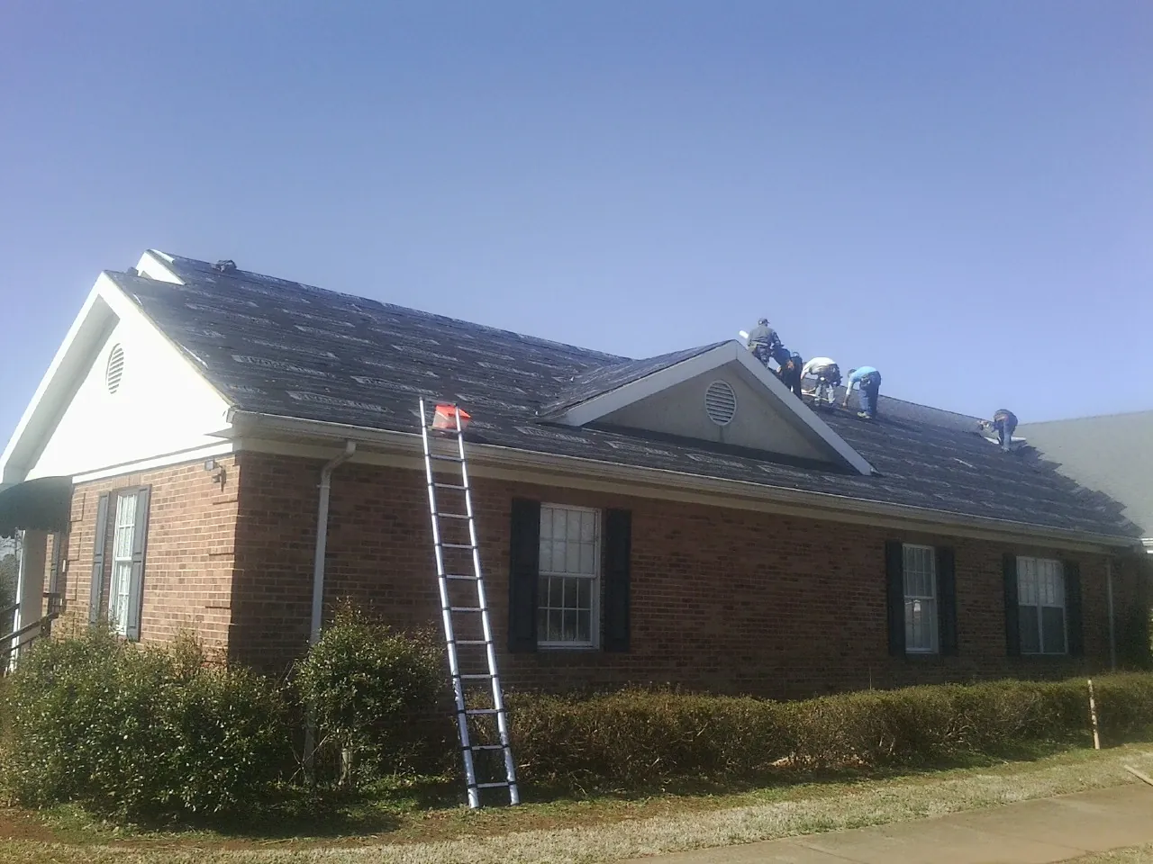 Crew tearing shingles off a brick ranch roof with a ladder set — Metal Roof Repair work by our crew in Wyncote