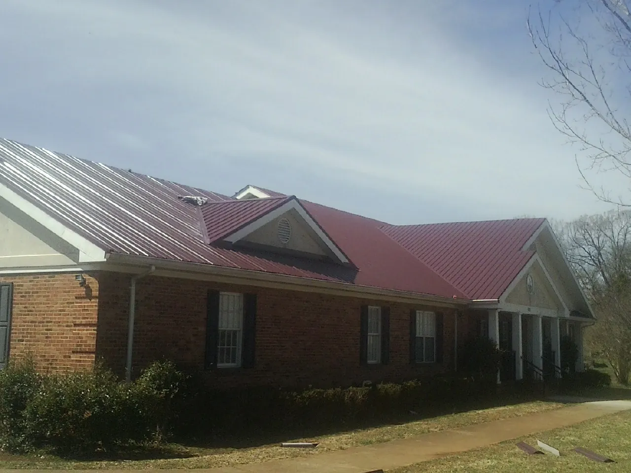 Red metal roof with gabled entries on a long brick building, from a Hail Damage Roof Repair job in Wyncote