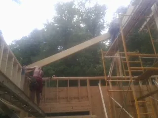 Carpenter raising a rafter beam on a new second story frame in Wyncote