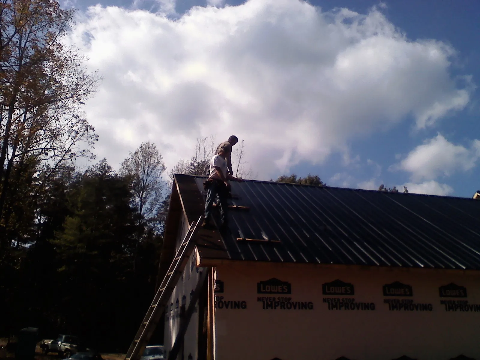 Roofer fastening dark metal panels high against a cloudy sky, from a Roof Inspection job in Wyncote
