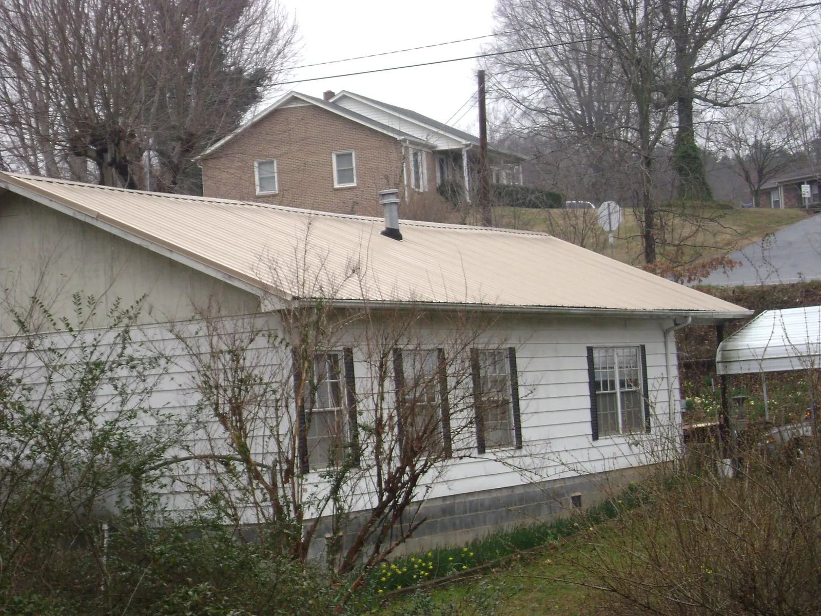 Tan metal roof on a white sided house set into a hillside — Commercial Roofing by Roofing Brothers in Wyncote